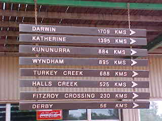 Sign reads: Darwin 1709k, Katherine 1395k, Kununurra 884k, Wyndham 895k, Turkey Creek 688k, Halls Creek 525k, Fitzroy Crossing 230k, Derby 56k